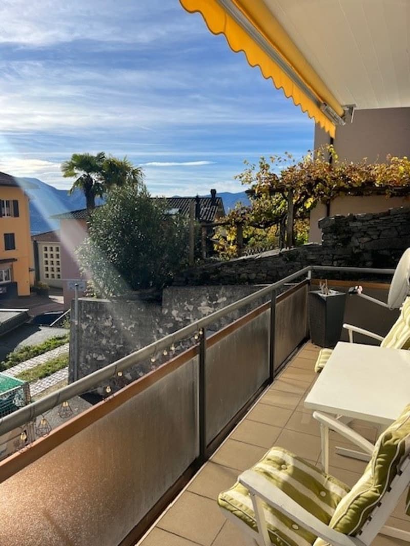 balcony with table and chairs, metal railing, green and yellow plants, mountain view