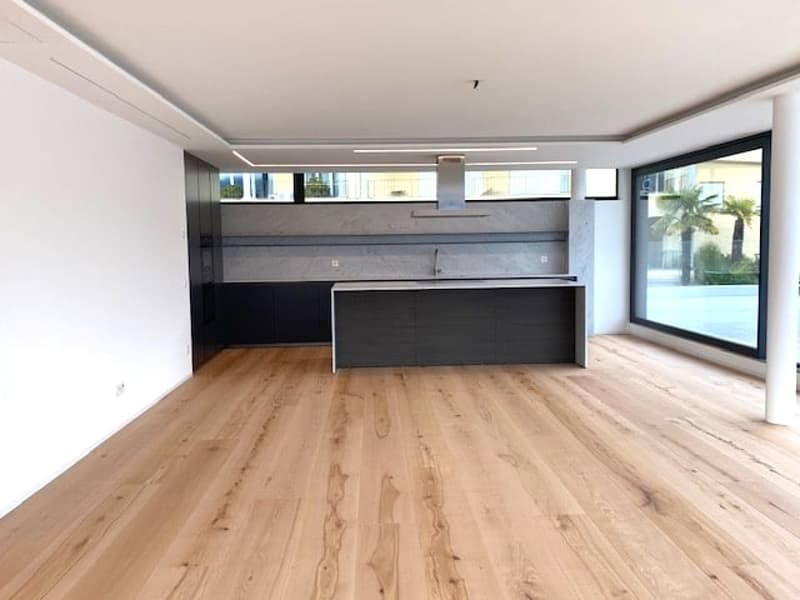 Large open-plan living space with hardwood flooring, black kitchen island, and large windows providing natural light