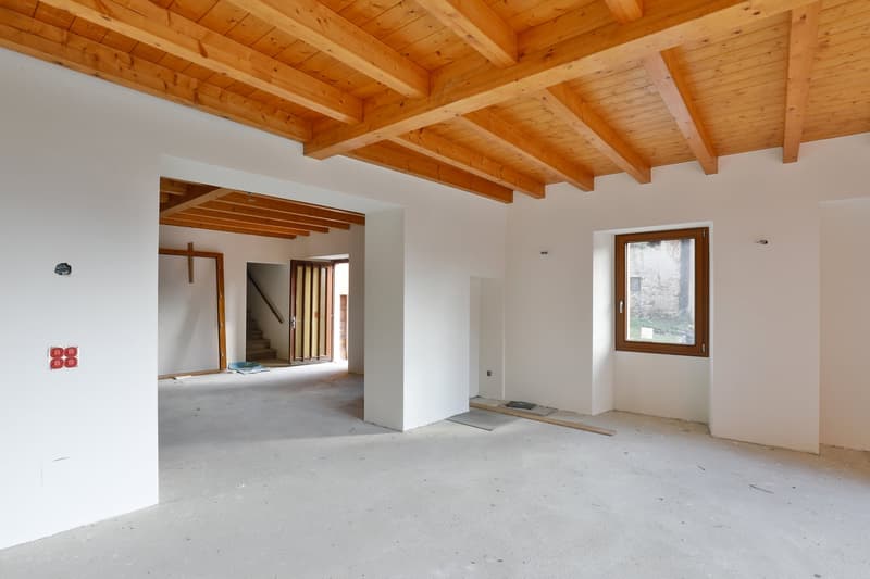open layout, unfinished interior, wooden beams, power outlet on wall, window on the right, open doorway in the middle, wooden staircase to the right of doorway