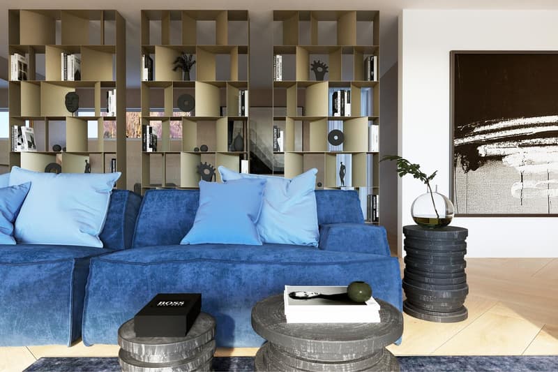 Large blue velvet sofa, built-in shelving unit with decorative objects, coffee table made of stacked tires, vase with plant, abstract artwork on the wall
