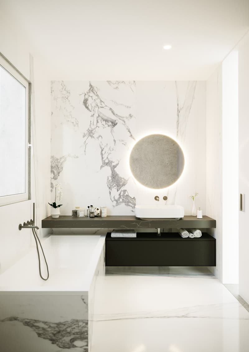 The image shows a modern and minimalist bathroom design. The walls are covered in a marble-like pattern, creating a sleek and elegant look. The vanity features a floating design with a dark wood finish, providing storage space. A round, backlit mirror is