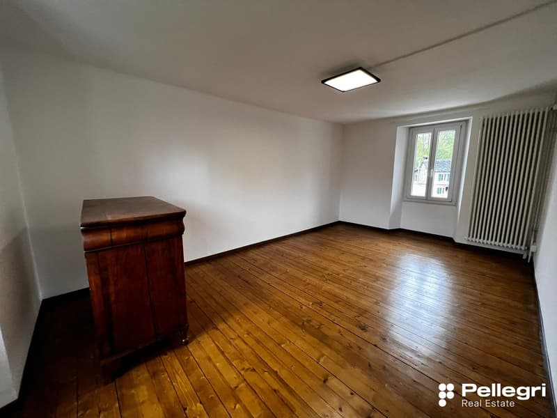 Spacious room with hardwood floors, white walls, and a large window. The room contains a wooden dresser or cabinet.