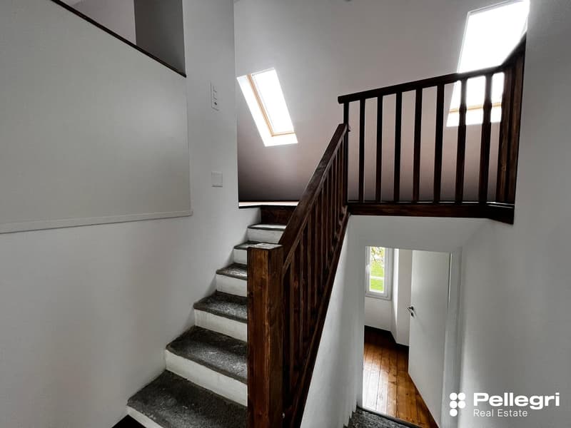 Wooden staircase with dark wooden railing, leading to an upper level with a window providing natural light.