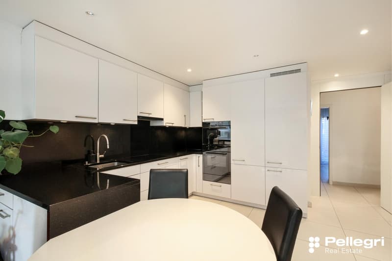 Modern, open-plan kitchen with white cabinets, black countertops, stainless steel appliances including a dishwasher, and a round dining table with black chairs.