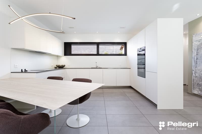 Modern, open-concept kitchen with white cabinets, black countertops, large window, built-in appliances including a dishwasher, and a dining table with chairs.
