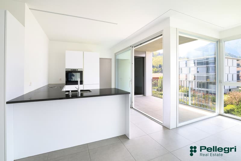 modern kitchen with island, black countertops, white cabinets, large windows, balcony