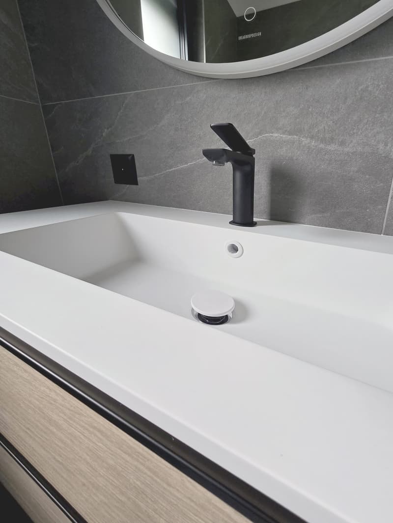 modern bathroom with a large white sink, black faucet, power outlet on the wall, large mirror