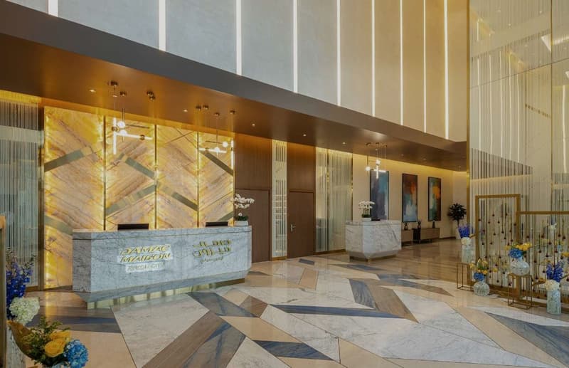 Modern design with marble flooring, golden wall designs, two reception desks, flower arrangements, lighting fixtures, framed art on wall