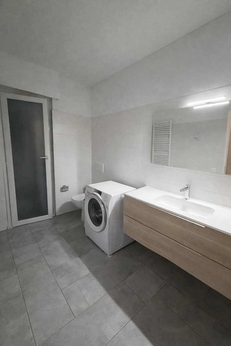 modern bathroom with white tiles, washing machine, sink, mirror, toilet