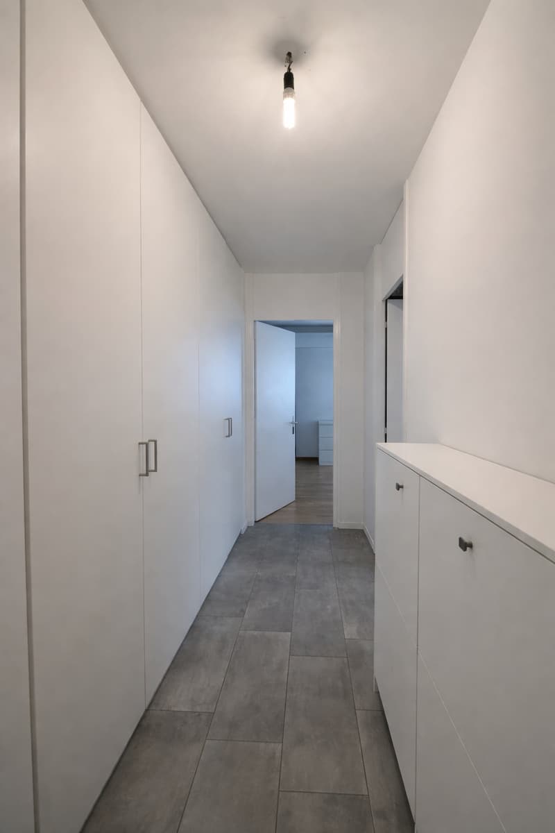 Empty hallway with white walls, gray tiles, and built-in cabinets on both sides.