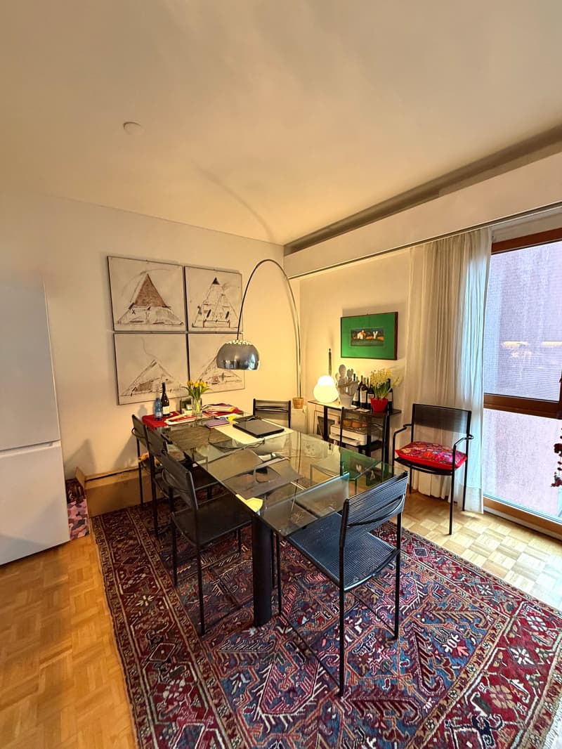 Dining room with a glass table, chairs, a rug, a lamp, a refrigerator, and a window with curtains