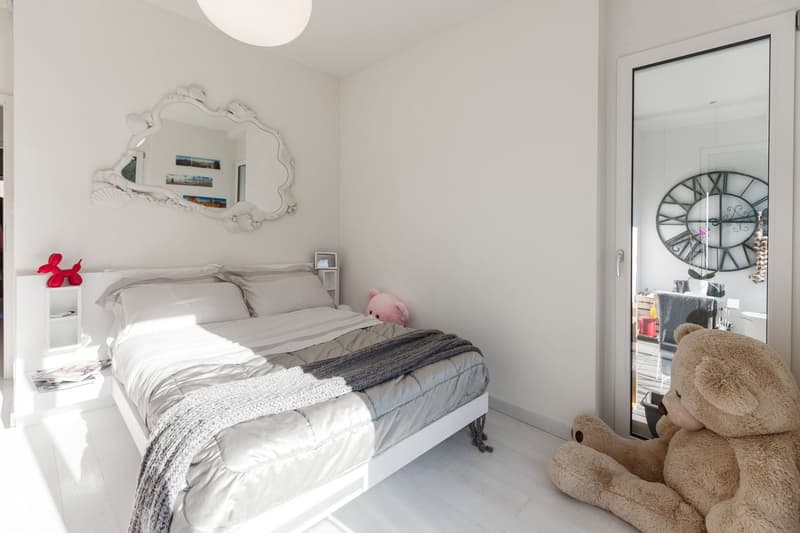 white walls, white bed, white nightstands, mirror, stuffed animals, open door