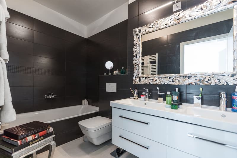 modern bathroom, white bathtub, white toilet, white sink, black tiles, mirror, toiletries