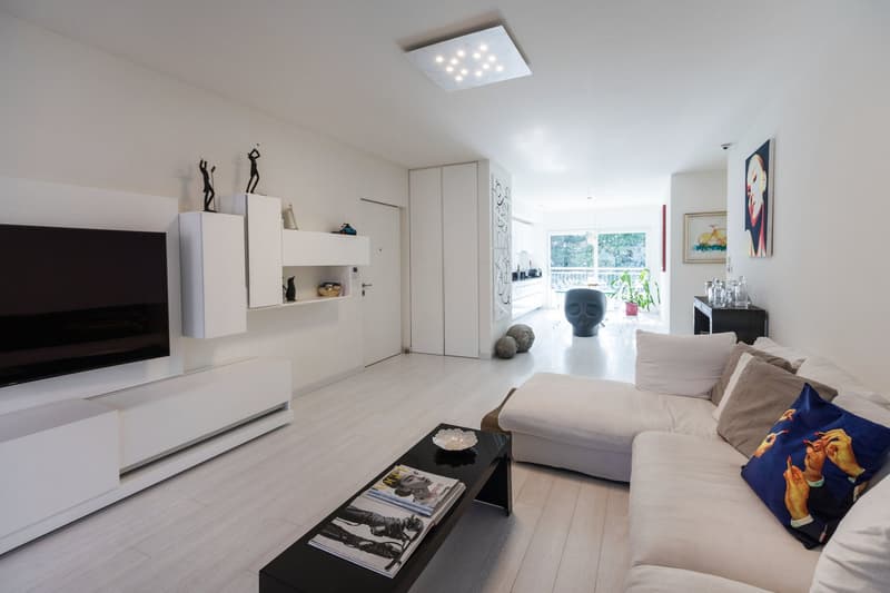 modern living room, white walls, white floor, large sofa, coffee table, flat screen TV, white cabinets, paintings