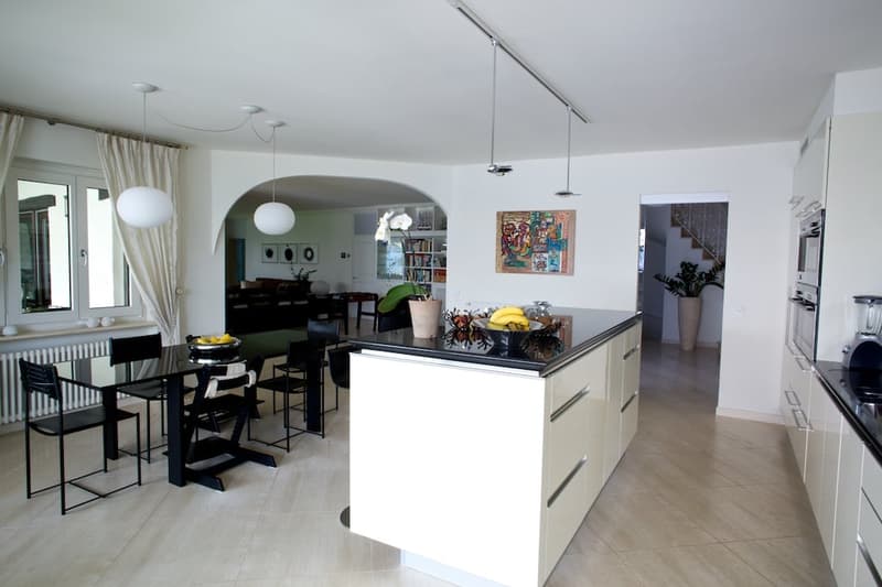 Open-concept kitchen and dining area with white cabinets, black countertops, and a kitchen island. The dining area has a black table and chairs. The space is well-lit with pendant lights and has a modern, minimalist decor style.