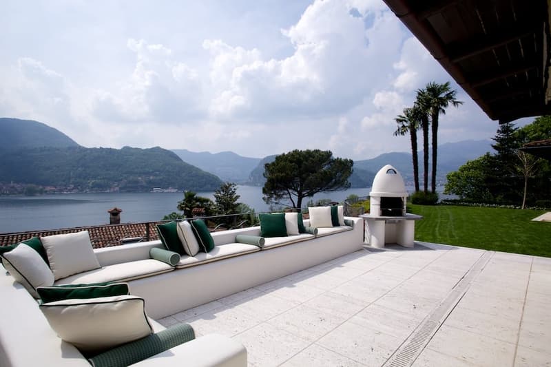 Spacious outdoor terrace with comfortable seating, a fireplace, and a scenic view of the lake and mountains in the background.