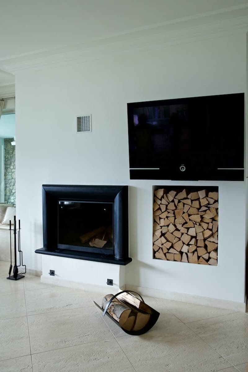 Modern living room with a black fireplace, a TV mounted on the wall, and a built-in storage unit filled with firewood.