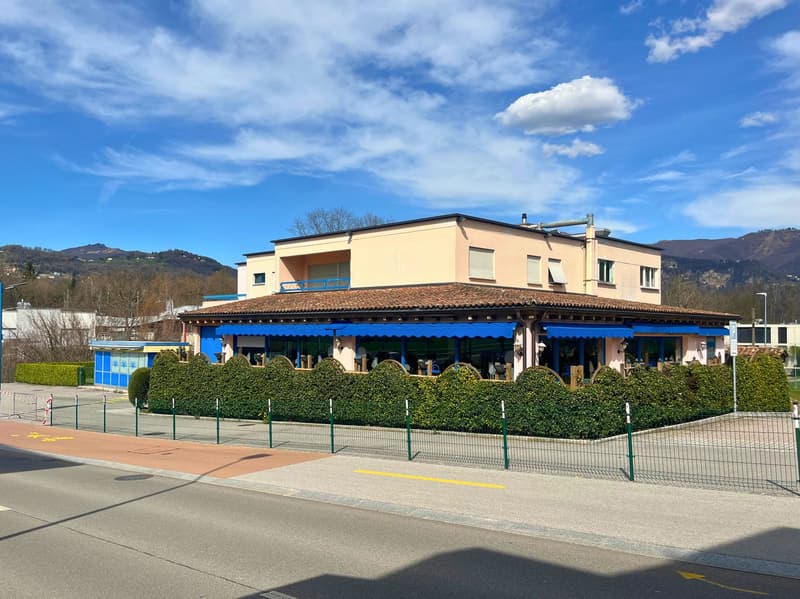 A building with two floors, with a brown roof, blue awnings, and green fencing around it.