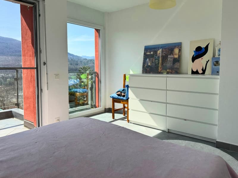 Spacious bedroom with large windows offering a scenic mountain view, white walls, gray bedding, white dresser, and artwork on the wall