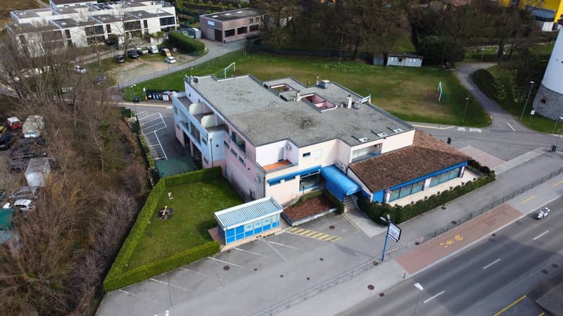 two story pink building, brown roof, blue roof with green walls, glass windows, cars parked