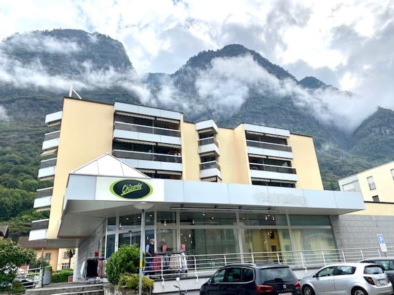 A multi-story commercial building with a parking lot in front, located in a mountainous area with clouds and fog in the background.