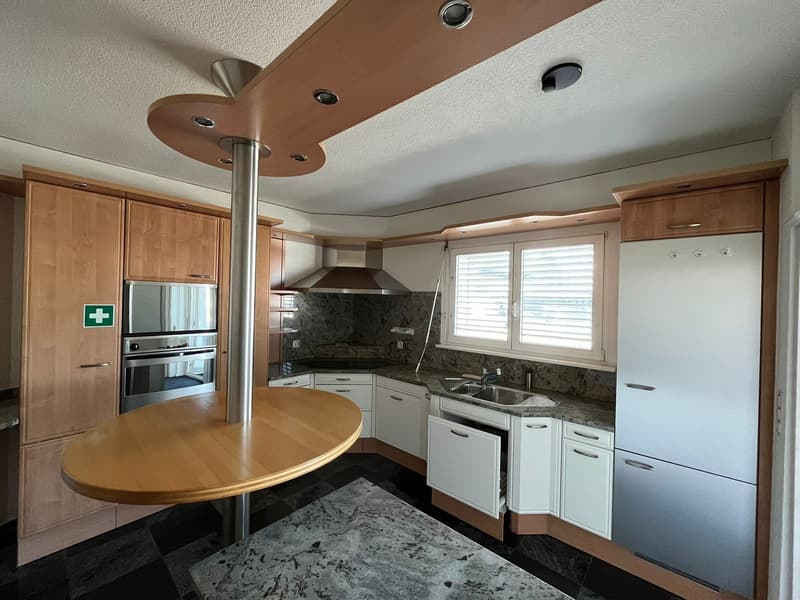 Spacious kitchen with wooden cabinets, granite countertops, built-in appliances including a dishwasher, and a round dining table.
