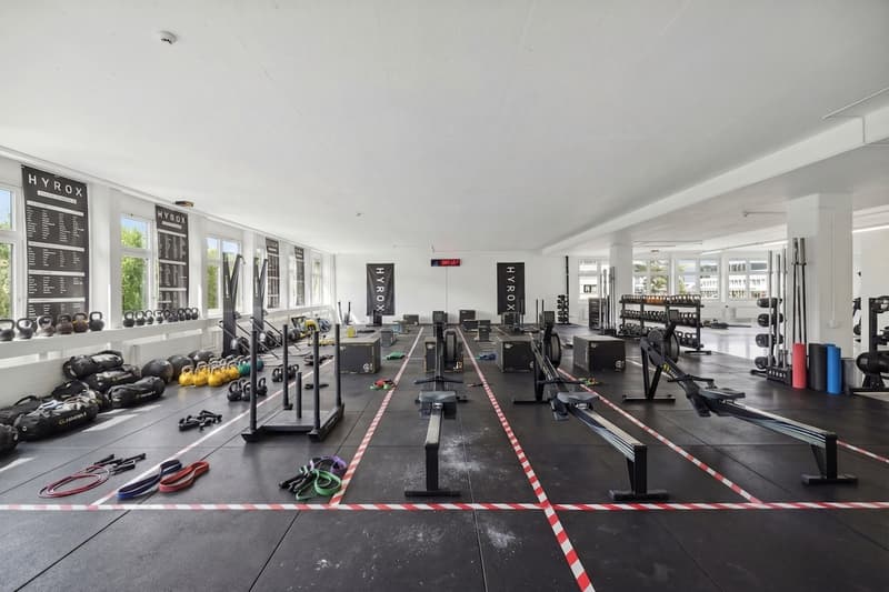 large gym room, various exercise equipment, weights, rowing machines, mats, windows