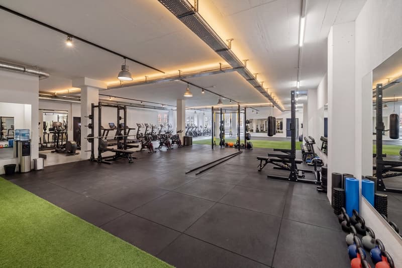 well-lit gym with various exercise equipment, mirrors, and a green mat area