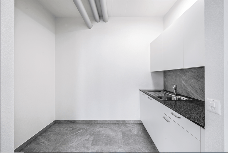 Minimalist kitchen with white walls, gray tile flooring, and a built-in dishwasher in the countertop