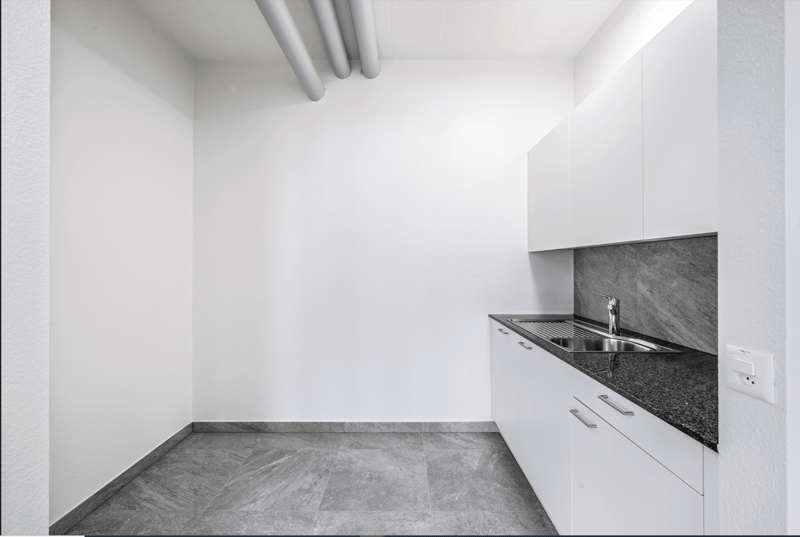 Minimalist kitchen with white walls, gray tile flooring, and a built-in dishwasher in the countertop