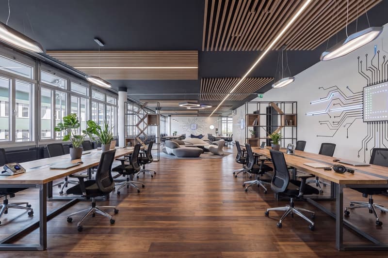 modern office with wooden floors, large windows, long desks, modern chairs, plants, and a lounge area
