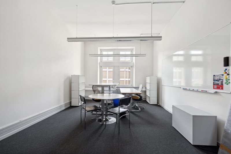 modern, white walls, carpeted floor, round tables with chairs, whiteboards, storage cabinets, open windows