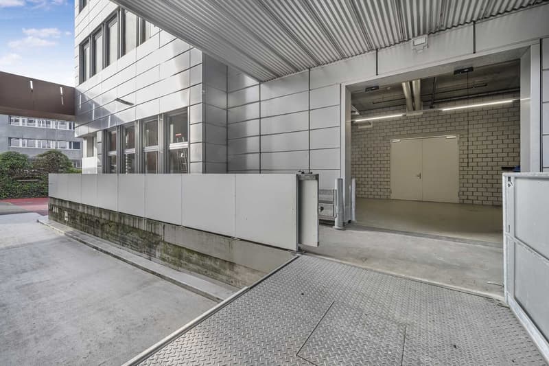 modern building with white metal panels, open parking garage, white and grey interior walls, paved lot
