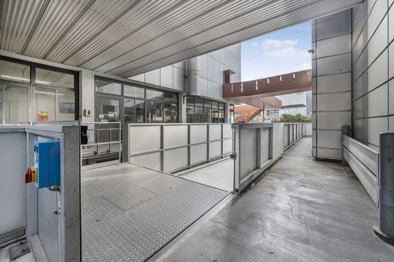 Stainless steel railings, metal ramp, grey concrete flooring, large window overlooking exterior, modern building design