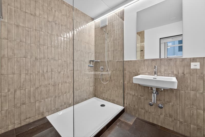 White shower cubicle, white sink, tiled walls, mirror