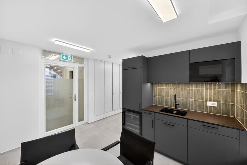 Modern kitchen with black cabinets, green tiles, stainless steel sink, white tile flooring