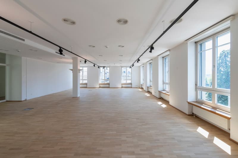 large room, wooden floor, white walls, multiple large windows, central lighting