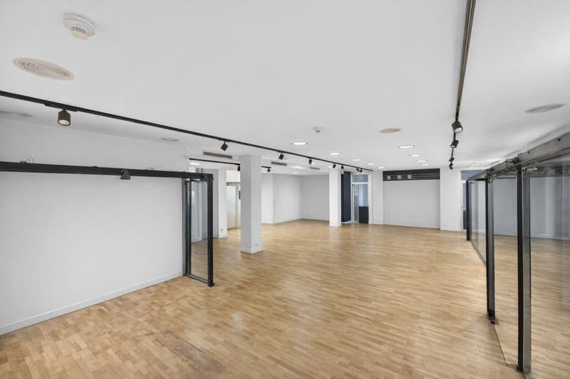 Empty office room with white walls, wooden floors, track lighting, sliding glass doors