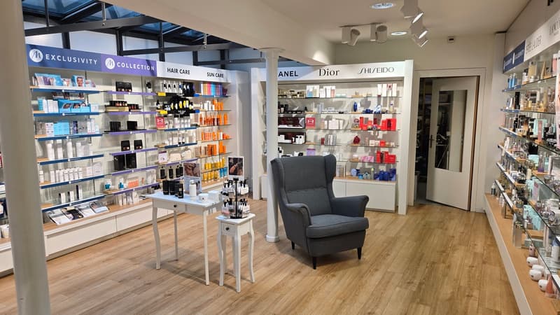 A store with wooden floors, white walls, shelves with products, a white table, and a gray armchair.