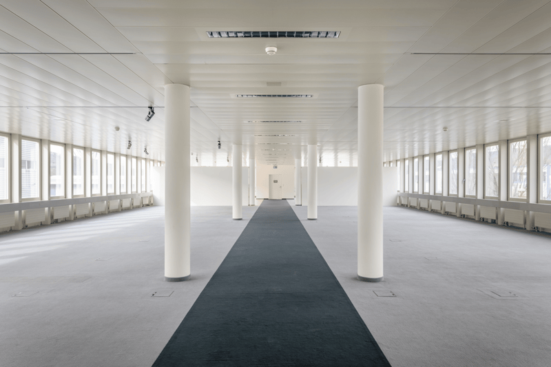 long hallway, white walls, gray floor, black carpet, white pillars, large windows, white ceiling