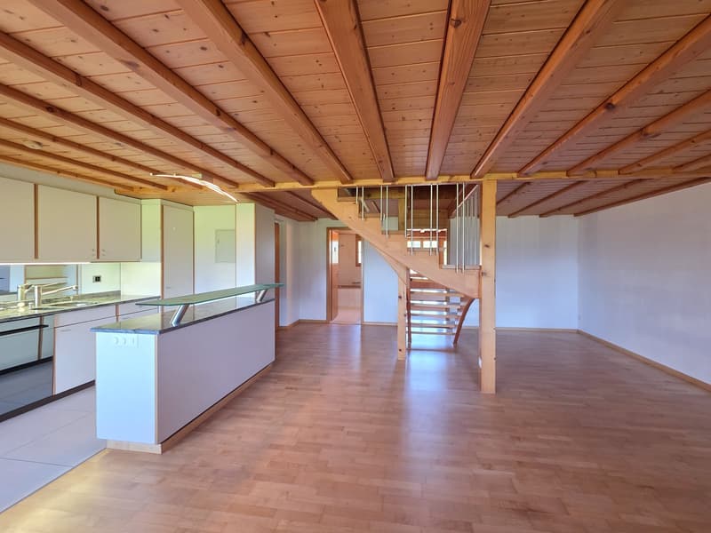 large empty room with high ceiling, wooden beams, white kitchen, white tiled floor, wooden stairs