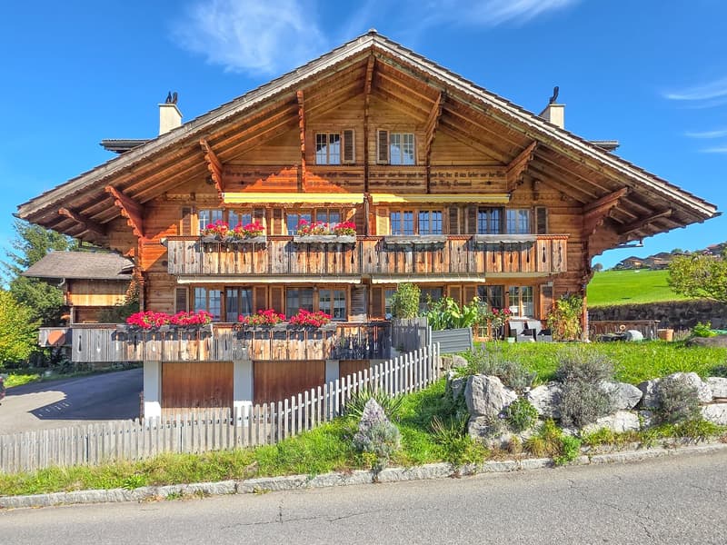 2 story wooden house, red flowers on balconies, fence in front, green grass, clear sky