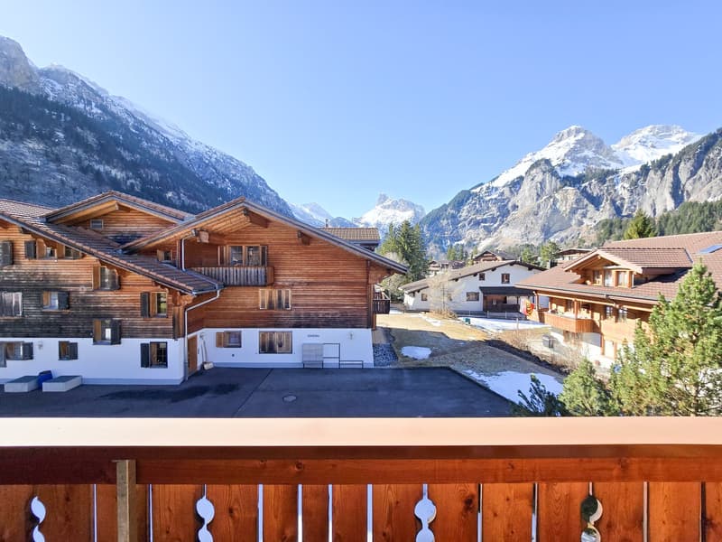 Wooden chalet, multiple windows, balcony, snow-covered mountains in the background