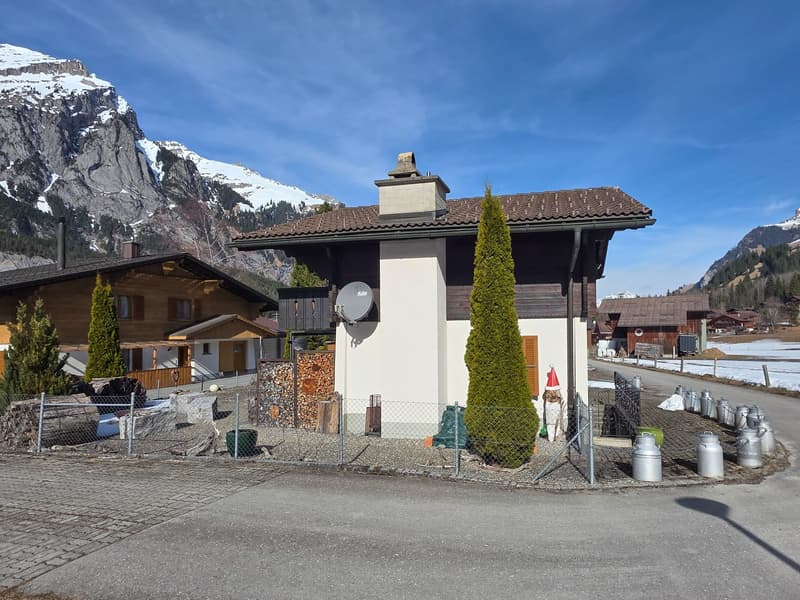 Detached house, brown roof, white walls, chimney, satellite dish, surrounded by mountains, wooden fence, gravel driveway