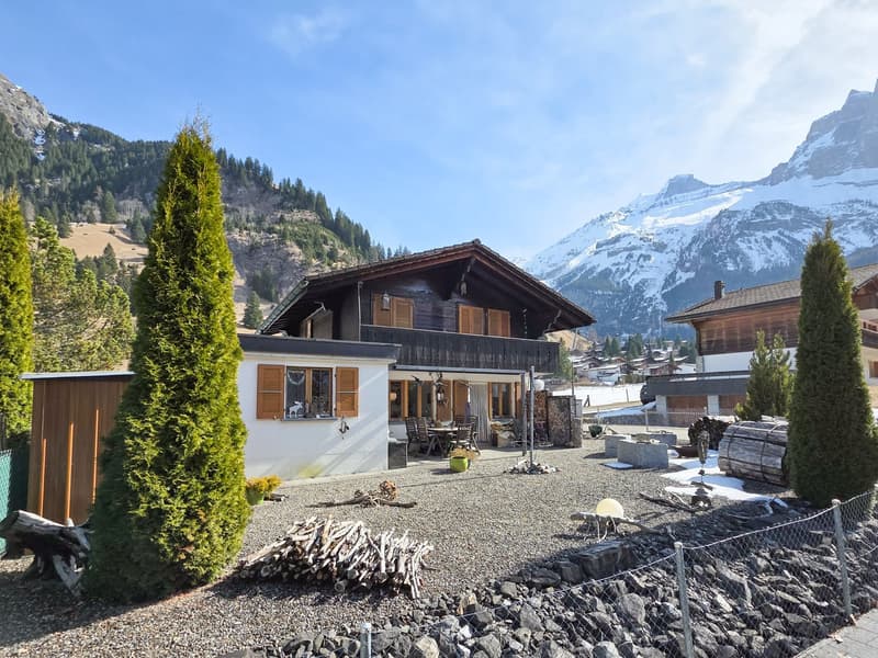 Mountain house, wooden exterior, large windows, balcony, outdoor seating, gravel driveway, trees, mountain view
