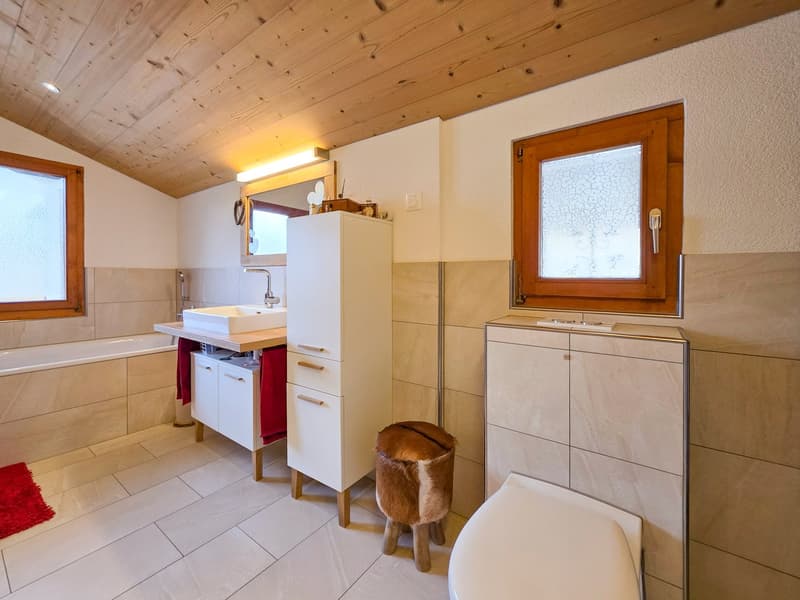 Bathroom with bathtub, sink, toilet, wooden ceiling, tiled floor, wooden stool, wooden window frames, white walls, mirror, and a wooden door.