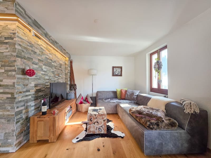 stone wall, wooden floor, gray sofa, coffee table, TV, wooden cabinet, lamp, picture frame, window