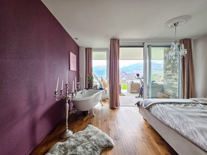 Purple wall, wooden floor, white bathtub, chandelier, bed, rug, sliding glass door, balcony, view of mountains