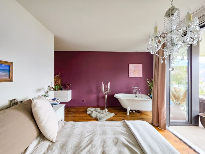 large bed, white sheets, pillows, purple wall, bathtub, chandelier, wooden floor, sliding glass door, balcony
