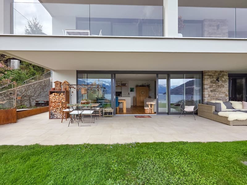 Modern house with glass walls, balcony, outdoor dining area, and a view of the mountains